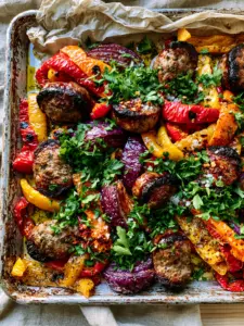 Close-up of roasted Italian sausage rounds with dark brown charred edges and juicy centers. (sausage and peppers recipe)