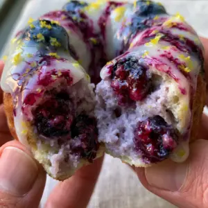 Close-up of a fluffy baked blueberry donut being pulled apart to reveal a moist purple interior crumb. (baked blueberry donuts)