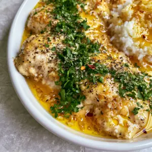 Close up of succulent sliced slow cooker chicken breast glistening with golden garlic butter sauce and fresh parsley.